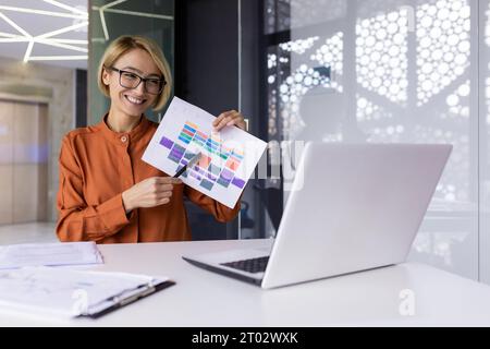 Giovane donna d'affari di successo ad una presentazione online, il dipendente sorride e mostra una macchina fotografica da tavolo con un computer portatile, soddisfatta dei risultati del risultato, video meeting online , Foto Stock