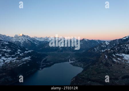 Foto di un drone nelle Alpi svizzere su un lago chiamato Walensee e sullo sfondo le vette delle montagne sono illuminate dal sole del mattino. Foto Stock