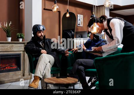 Durante la vacanza invernale potrete sedervi e conversare nell'area lounge della stazione sciistica mentre il cameriere serve caffè. I visitatori apprezzano la calda hall dell'hotel prima di raggiungere le montagne innevate e prepararsi per attività di snowboard. Foto Stock