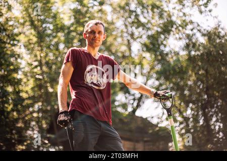 Ritratto di uomo felice giardiniere che tiene la pala mentre in piedi nel giardino in estate Foto Stock