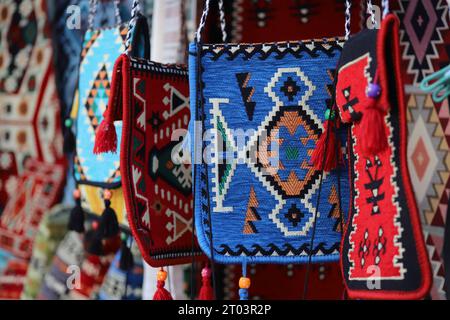 Una fila irregolare di audaci borse a spalla in stile tappeto o tappeto con nappine e perline, con motivi geometrici misti, multicolori, look etnico, tappeto intrecciato o tappeto. Foto Stock