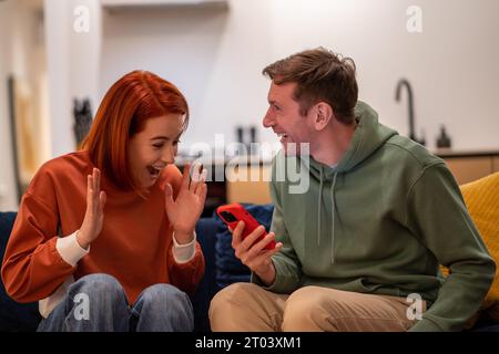 Felice felicissimo uomo di coppia donna che legge buone notizie sullo smartphone seduto sul divano a casa. Foto Stock
