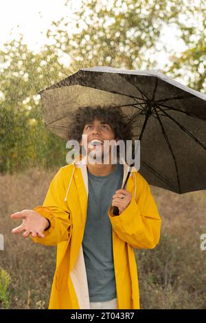 Bellissimo uomo arabo che tiene un ombrello mentre passeggia all'esterno. Guarda la fotocamera con vera gioia e sorriso sincero. Foto Stock