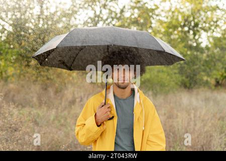 Ragazzo arabo che tiene l'ombrello mentre passeggia all'esterno. Guarda la fotocamera con vera gioia e sorriso sincero. Foto Stock