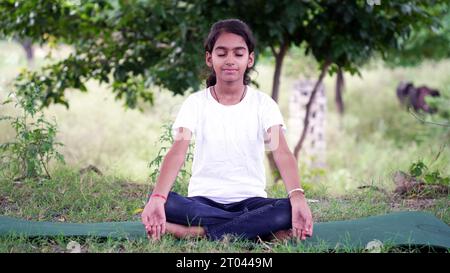 Incantevole bambina che fa una seria meditazione yoga in giardino. Piccola ragazza indiana che fa meditazione Foto Stock