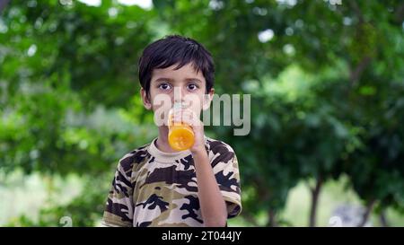 Ragazzo che beve succo. Ragazzo asiatico che beve da una bottiglia di plastica. Ritratto di un ragazzo che beve succo d'arancia. Succo d'arancia in bottiglia. La gente beve energia Foto Stock
