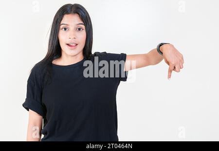 Stupita ragazza latina che indica una pubblicità. Ragazza allegra che punta la pubblicità verso il basso. Persone latine che puntano verso il basso uno striscione Foto Stock