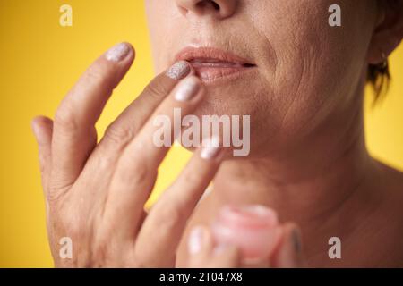 Immagine ritagliata di donna matura che applica il balsamo per le labbra per idratare la pelle Foto Stock