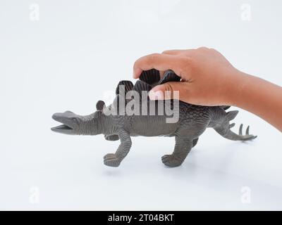 le mani dei bambini giocano a stegosaurus toy, genere di dinosauro corazzato isolato su sfondo bianco Foto Stock