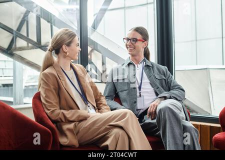 due colleghi eleganti che indossano abiti eleganti seduti su sedie rosse e guardarsi l'un l'altro, coworking Foto Stock