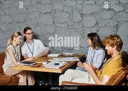 quattro giovani colleghi in abbigliamento business casual che fanno i loro documenti al tavolo, concetto di coworking Foto Stock