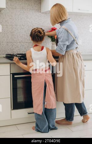 Una giovane madre e sua figlia cucinano i pancake insieme per colazione. La madre insegna alla figlia a cucinare. Foto Stock