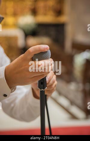 Uomo che tiene in mano e prepara il microfono da utilizzare nelle prestazioni musicali. Ambiente interno rustico, ad esempio tempio o chiesa. Primo piano Foto Stock