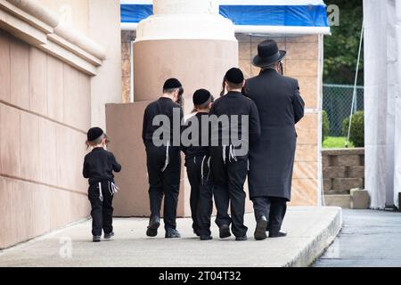 Un padre e i suoi 4 figli vestiti identicamente camminano su una pendenza per partecipare a un servizio sinagogico. A Kiryas Joel, Orange County, New York. Foto Stock