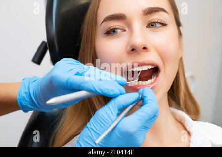 Paziente seduta su sedia durante le procedure dentistiche in clinica odontoiatrica. Il dentista controlla i denti anteriori con l'ausilio dell'attrezzo a specchio e controlla la resistenza dei denti Foto Stock