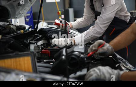 I tecnici di riparazione auto utilizzano un multimetro di tensione per lavorare nei negozi di riparazione auto Foto Stock