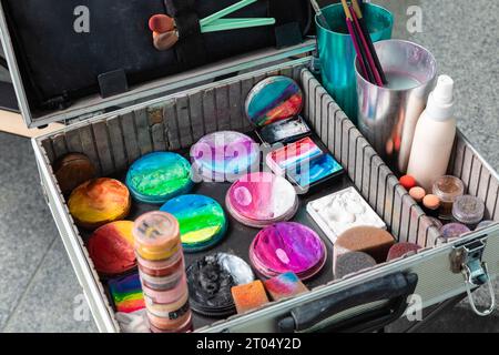 Un'immagine ravvicinata cattura una valigia aperta in metallo argento, rivelando una serie di colori vivaci per il viso, invitando infinite possibilità creative Foto Stock