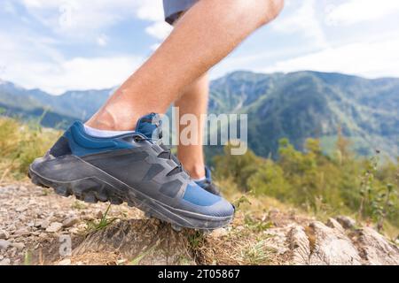 Gambe in movimento, stinci e piedi nelle scarpe da ginnastica, un escursionista maschile che cammina in salita su un sentiero sterrato attraverso la foresta da vicino. Concetto escursionistico estivo. Foto Stock
