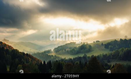 Paesaggio montuoso nebbioso autunnale con raggi del sole mattutino che brillano tra le nuvole. La regione di Orava in Slovacchia, Europa. Foto Stock