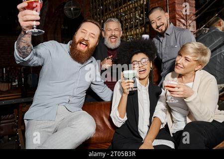 eccitati amici multietnici che tengono un drink e ridono nel cocktail bar, divertendosi dopo il lavoro Foto Stock