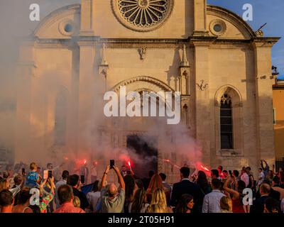 il fumo riempie l'aria dai riflessi rossi mentre una festa di nozze celebra il sole della prima sera di fronte alla cattedrale di sibenik Foto Stock