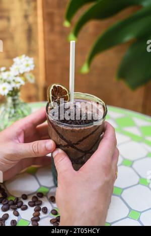 Bere a mano cacao con burro di banana e arachidi su un tavolo con vaso di fiori Foto Stock