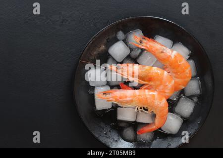 Gamberi grandi refrigerati in un piatto con ghiaccio su sfondo scuro. Gamberi bolliti in un piatto nero con ghiaccio, vista dall'alto. Frutti di mare su ghiaccio tritato, eati salutari Foto Stock