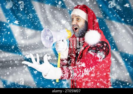 Babbo Natale grida in un corno e mostra un gesto aggressivo con la mano sullo sfondo della bandiera bavarese. Foto Stock