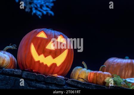 Un sorridente Jack o Lanterna seduto su un vecchio portico di legno con piccole zucche e foglie cadute come Halloween. Foto Stock