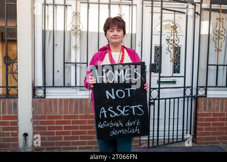 Londra, Regno Unito. 4 ottobre 2023. Una donna sta fuori casa con il cartello "Homes Not Assets". Nell'ottobre 2023 il Consiglio di Bexley ha approvato i piani per l'associazione Peabody Housing per costruire fino a 1.950 nuove case a South Thamesmead, il 35% delle quali è proposto per essere accessibile. Tuttavia, i residenti della Lesnes Estate stanno protestando contro la demolizione delle loro case esistenti. (Immagine di credito: © Velar Grant/ZUMA Press Wire) SOLO USO EDITORIALE! Non per USO commerciale! Foto Stock