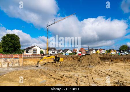 Lavori di scavo in un cantiere con escavatori e gru a torre. Area residenziale sotto il cielo blu con nuvole bianche. Foto Stock