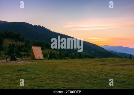 tramonto sulle montagne dei carpazi. lontana valle rurale con dolci colline tra pendii boscosi in un'atmosfera nebbiosa. rifugio in legno sul meado erboso Foto Stock