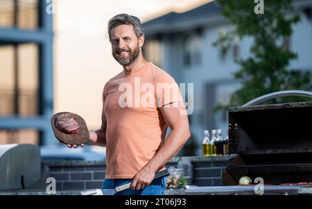 Uomo che si diverte a fare barbecue. Preparazione alla griglia con guru affumicato. uomo che grigia le sue carni preferite. cuoco che mostra le sue tecniche di barbecue durante l'evento di cucina. Foto Stock