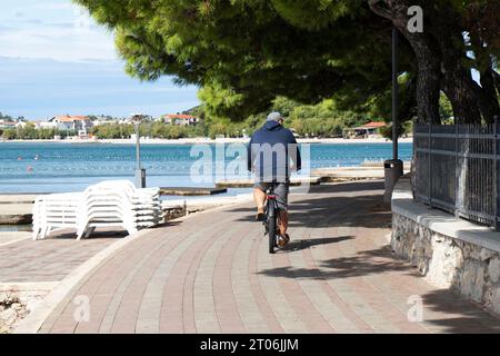 Vodice, Croazia - 24 settembre 2023: Persona in bicicletta al lungomare sulla spiaggia di fine stagione, da dietro Foto Stock