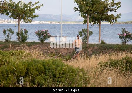 Vodice, Croazia - 16 settembre 2023: Giovane senza camicia jogging da solo sulla strada in riva al mare al mattino Foto Stock