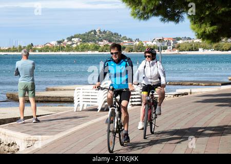 Vodice, Croazia - 24 settembre 2023: Coppia matura in bicicletta sulla passeggiata lungo la spiaggia Foto Stock