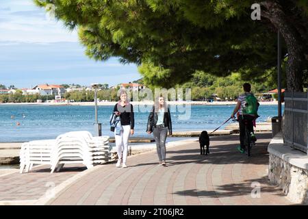 Vodice, Croazia - 24 settembre 2023: Persone che camminano e vanno in bicicletta sulla passeggiata lungo la spiaggia al tramonto in bassa stagione Foto Stock