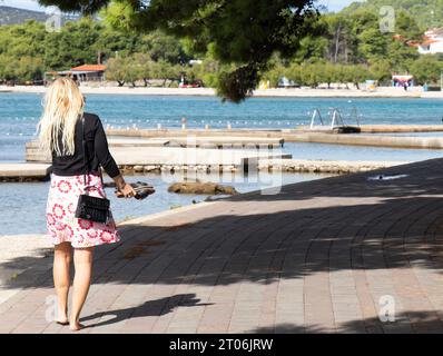 Vodice, Croazia - 24 settembre 2023: Donna bionda che cammina e va in bicicletta sul lungomare vicino alla spiaggia al tramonto in bassa stagione Foto Stock