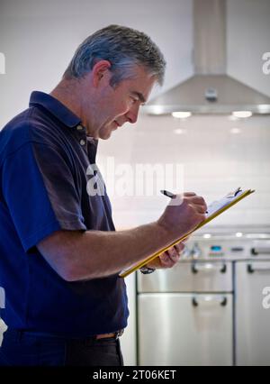 Man Property Sales Survey clipboard emissioni di carbonio progettazione delle vendite, manutenzione e rinnovo preventivo, in cucina domestica contemporanea Regno Unito Foto Stock