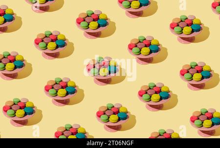 Fantasia colorata fatta di vari macaron su sfondo giallo pastello. Concetto minimale di dolce. Sfondo con motivo di biscotti macaron alla moda. Foto Stock