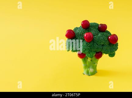Albero da frutto composto da broccoli verdi e ciliegie rosse su sfondo giallo pastello. Concetto creativo di frutta e verdura. Disposizione minima dei broccoli. Foto Stock