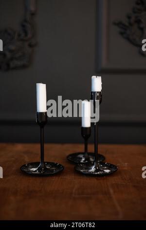 Tre moderni candelabri di vetro nero con candele bianche su un tavolo di legno in stile antico su sfondo scuro. Decorazioni eleganti e minimaliste con candele Foto Stock