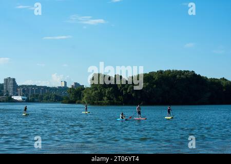 Persone non identificate cavalcano tavole SUP sul tranquillo fiume in estate nelle giornate di sole. Gli amici di gruppo trascorrono del tempo insieme, fanno un SUP sul fiume in città. Ucraina Foto Stock