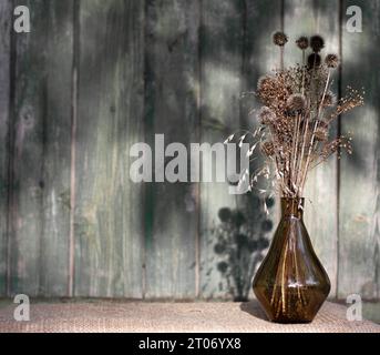 bouquet di fiori secchi ed erbe in vaso di vetro su sfondo di parete di legno. Natura morta in stile rustico. Luce dura. Cartolina con spazio per il testo. Foto Stock