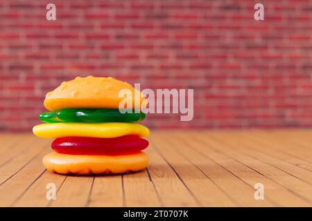 Layout creativo di grandi hamburger con colorate caramelle gommose sullo sfondo della parete di mattoni rossi. Concetto di cibo minimale. Composizione gustosa di dolci in gelatina. Foto Stock