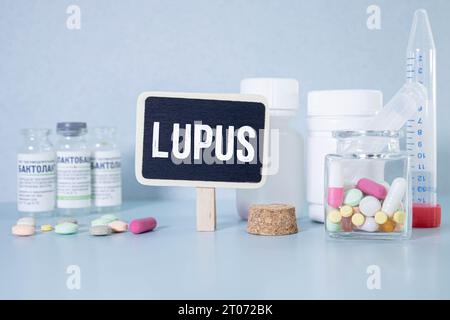 Medecine Concept - lavagna con testo Lupus, libro, pillole e stetoscopio su sfondo di legno blu. Foto Stock