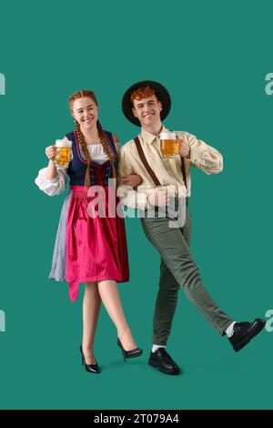 Giovane coppia in abiti tradizionali tedeschi con birra che balla su sfondo verde Foto Stock