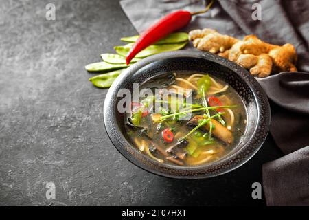 Zuppa di verdure asiatica con spaghetti, funghi, piselli da zucchero, nori, zenzero e peperoncino, tradizionalmente condito con pasta di miso in un recipiente di ceramica nera su un Foto Stock