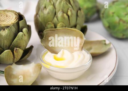 Deliziosi carciofi cotti con gustosa salsa serviti al tavolo, primo piano Foto Stock