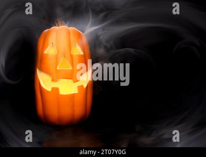 Zucche luccicanti scolpite di Halloween con nebbia affumicata e volti spaventosi su sfondo scuro. Foto Stock